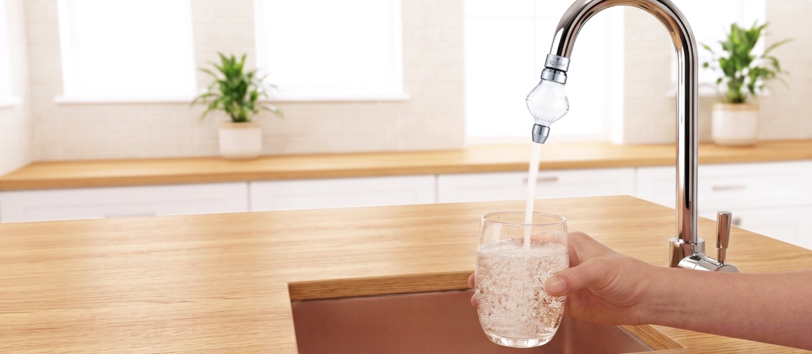 Hand holding a glass under a streaming chrome kitchen faucet with water flowing in.
